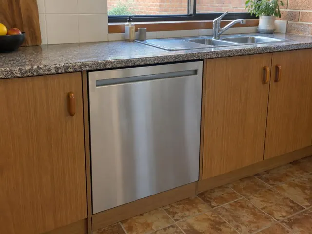 Built-in stainless dishwasher under a stone kitchen benchtop with timber cabinets in Croudace Bay
