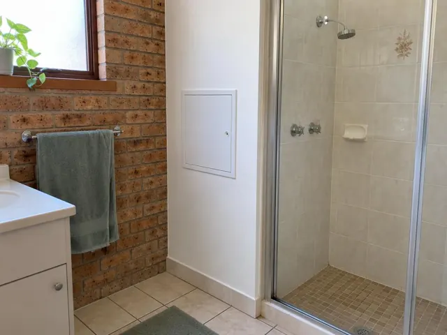 Bathroom wall with a small access panel beside a tiled shower and towel rail in Mount Hutton